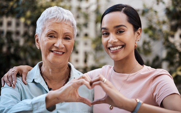 older mom with older daughter standing with hands connected in heart shape